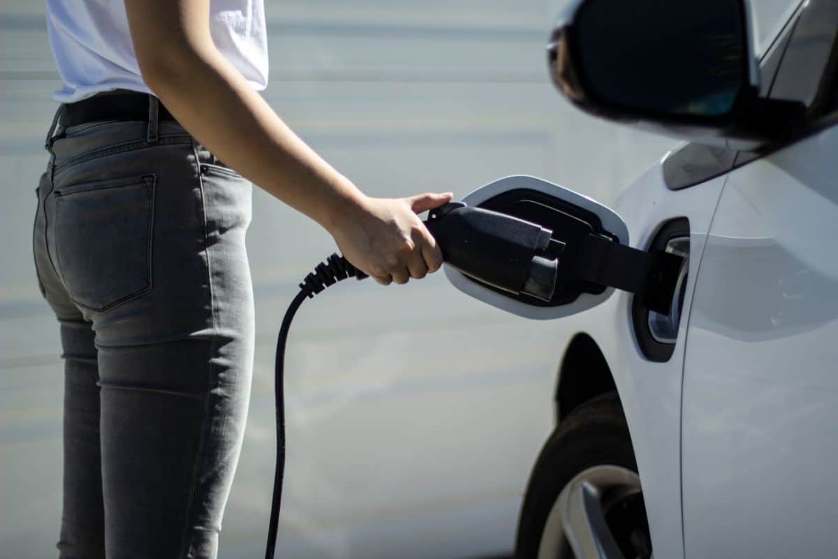 photo of a woman plugging charger in to the charging socket of a white electric vehicle passenger car