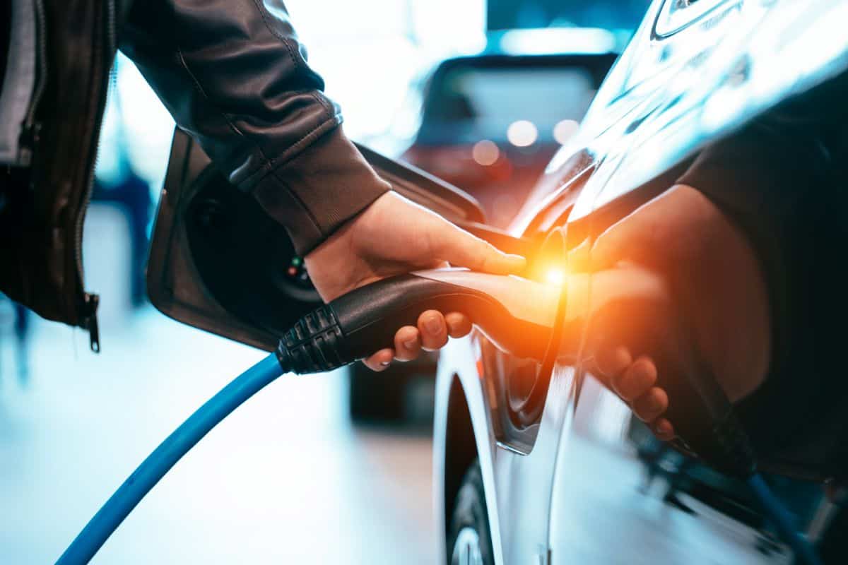 man plugs in charger to his electric car