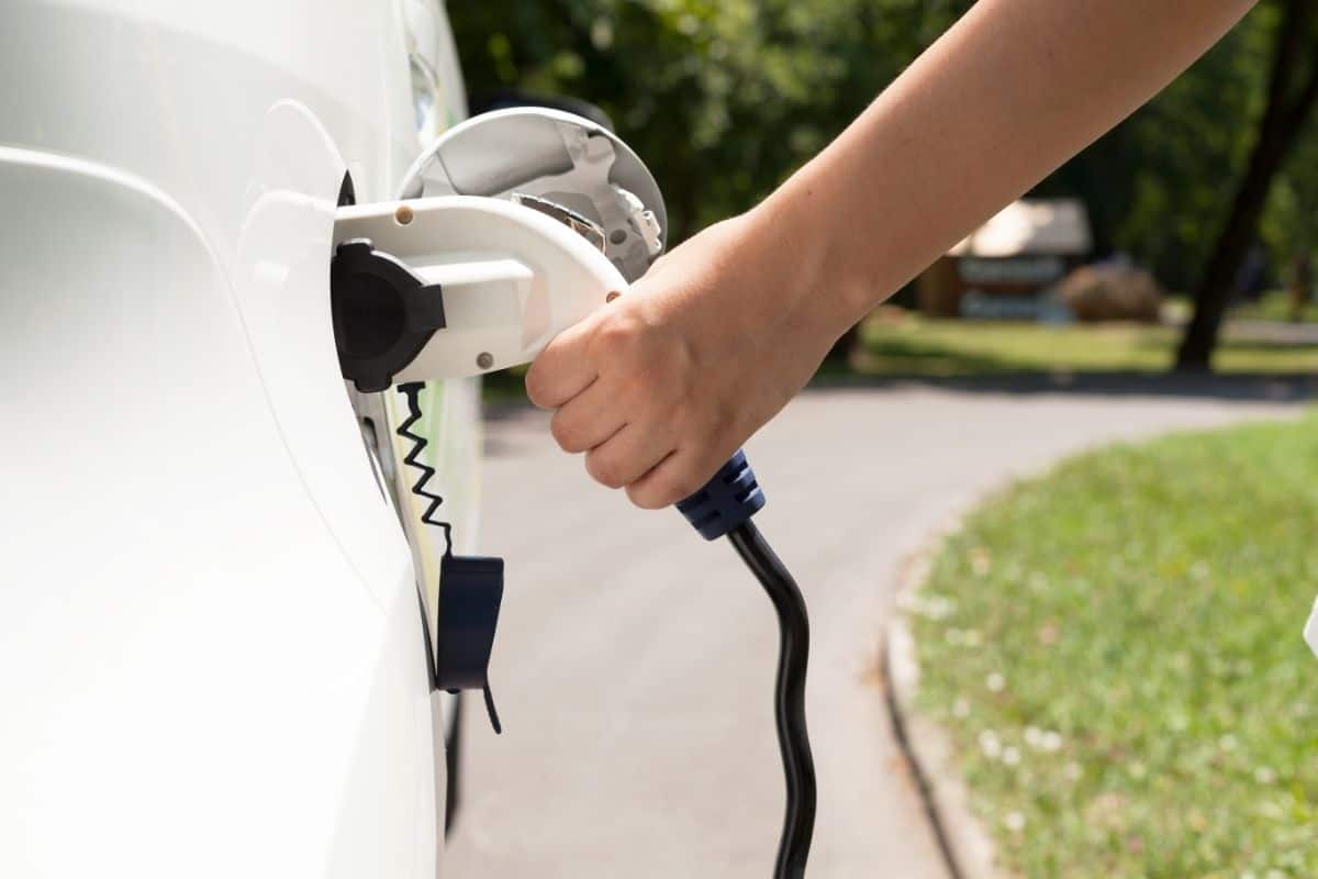 photo of someone inserting charging plug into charging socket of white electric vehicle car at roadside charging station