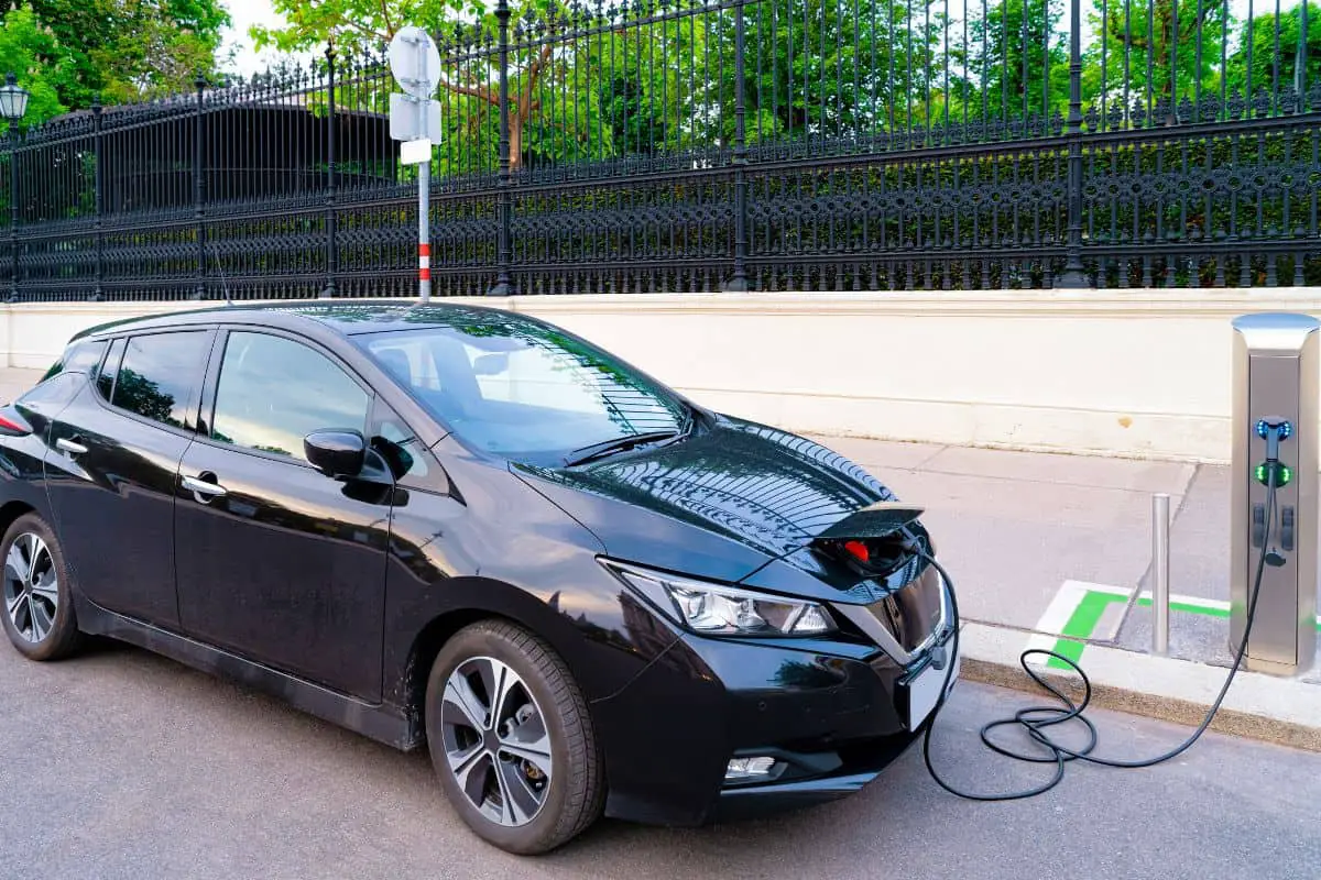 photo of a black electric car nissan leaf being charged on the street with a street charger