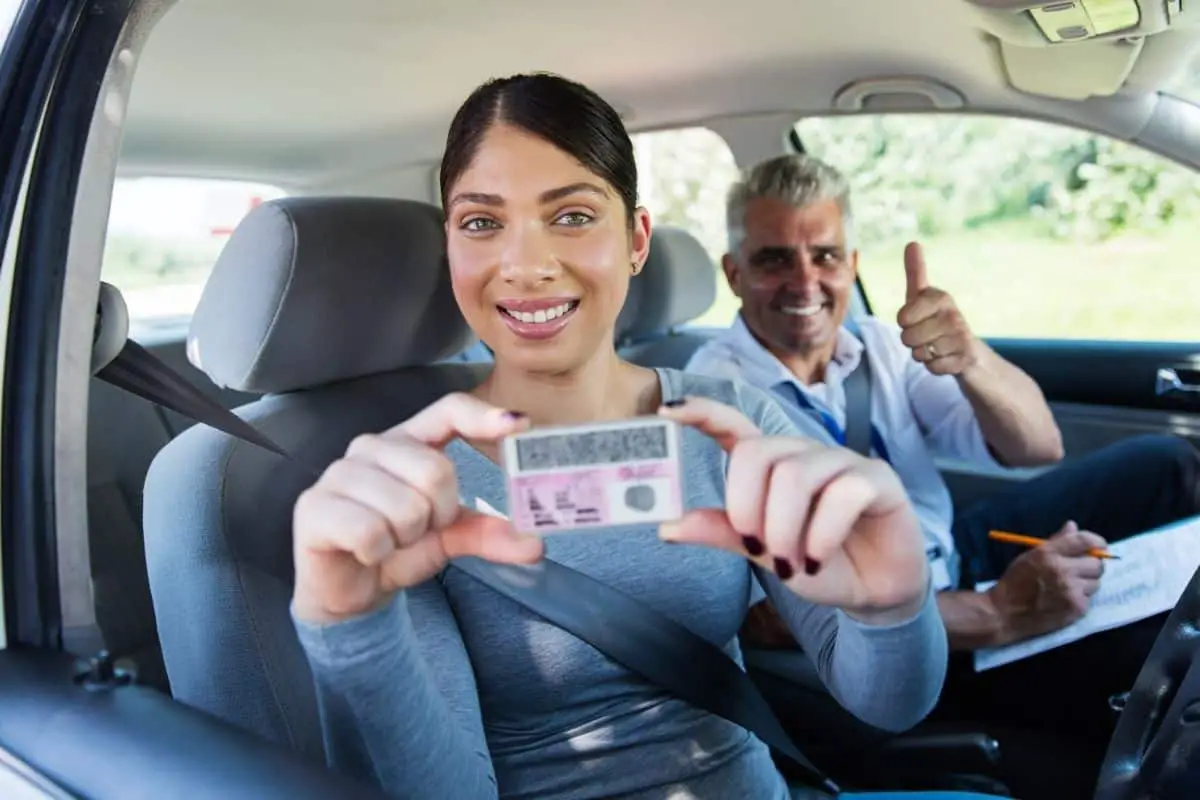 smiling young woman holding up her new california driving license after passing her driving test