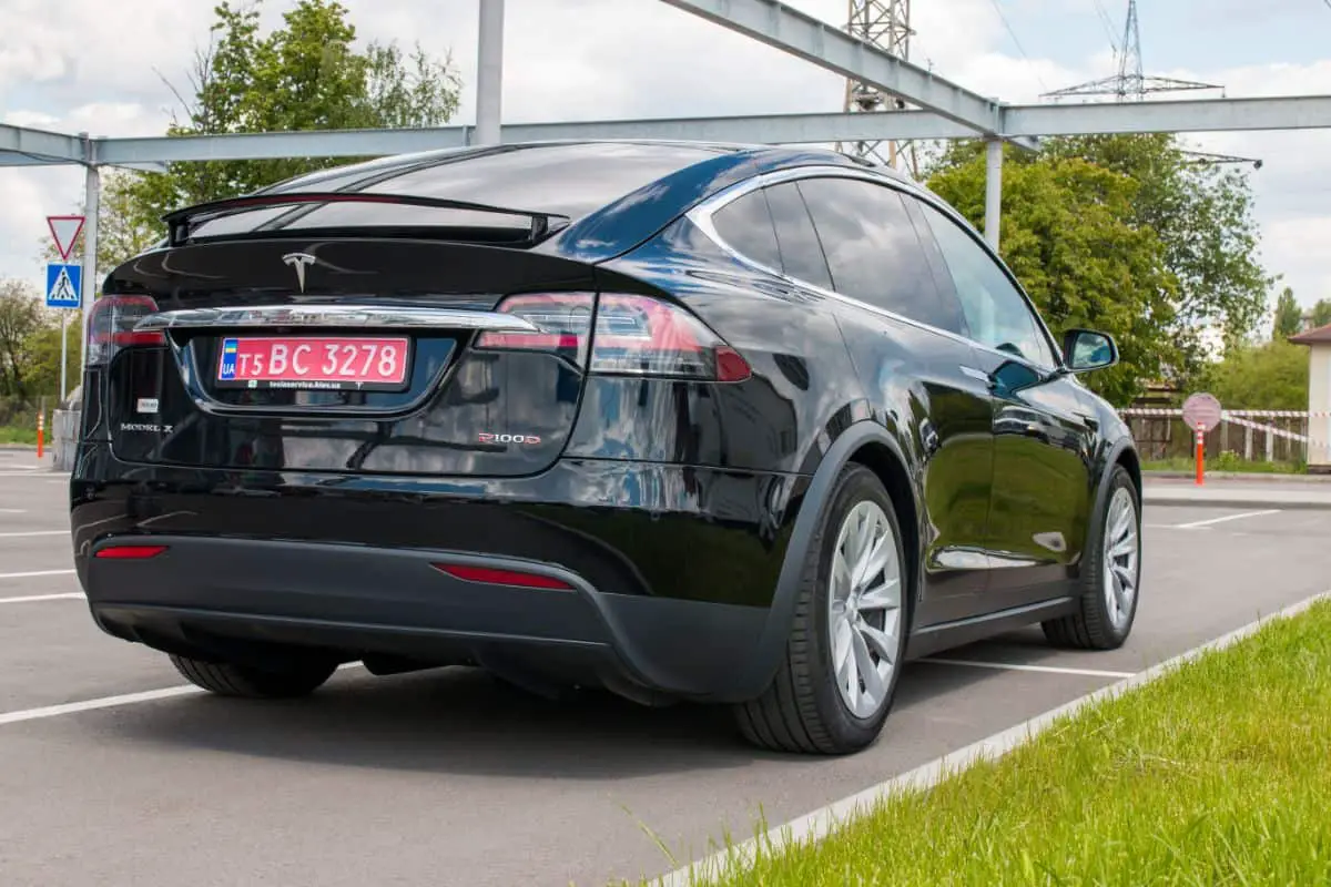 photo of a black Tesla electric car parked on a parking lot beside some grass