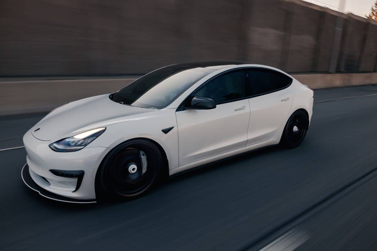 photo of a white tesla electric car driving on the road with natural motion blur of background