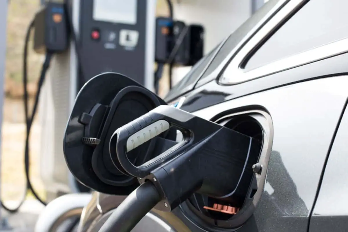 photo of charging plug inserted into charging socket of dark gray electric vehicle car parked at charging station