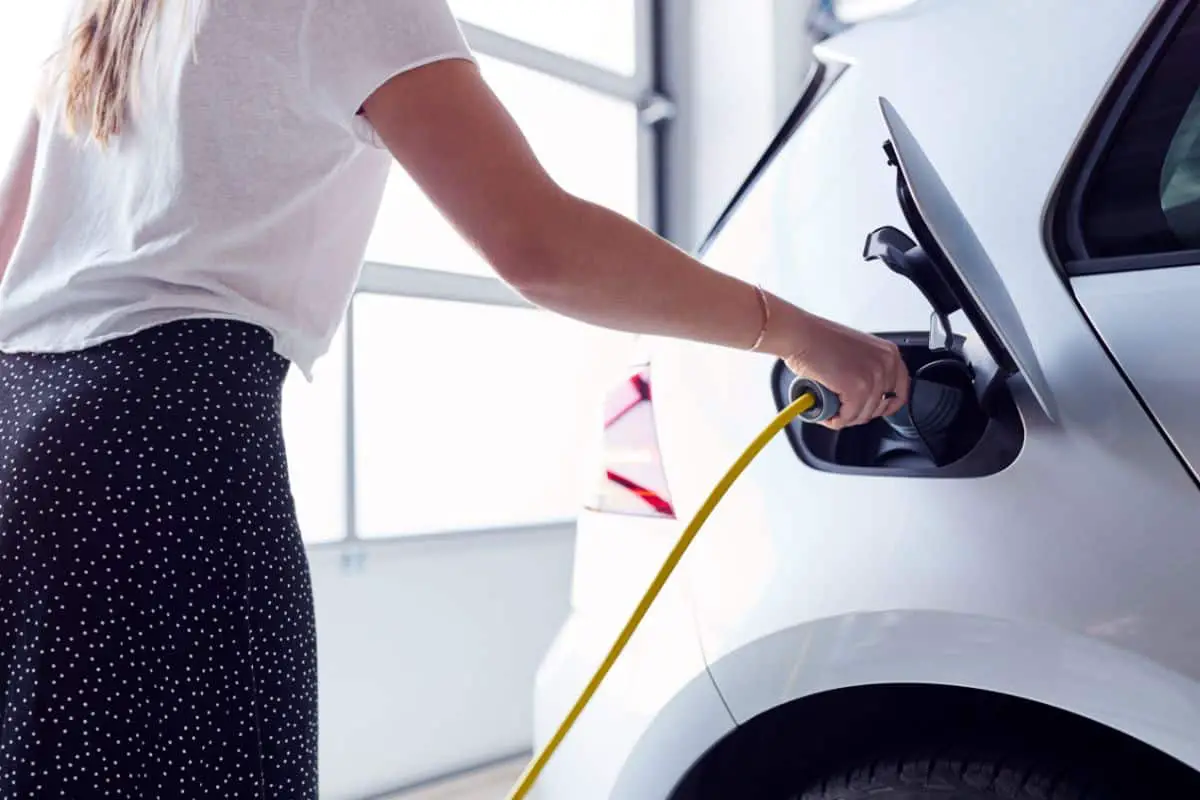 photo of a woman inserting a charging plug into the charging socket of a white electric vehicle car
