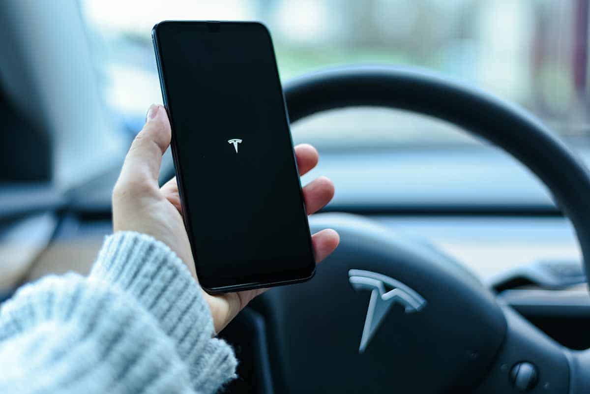 holding cell phone displaying tesla logo inside tesla car