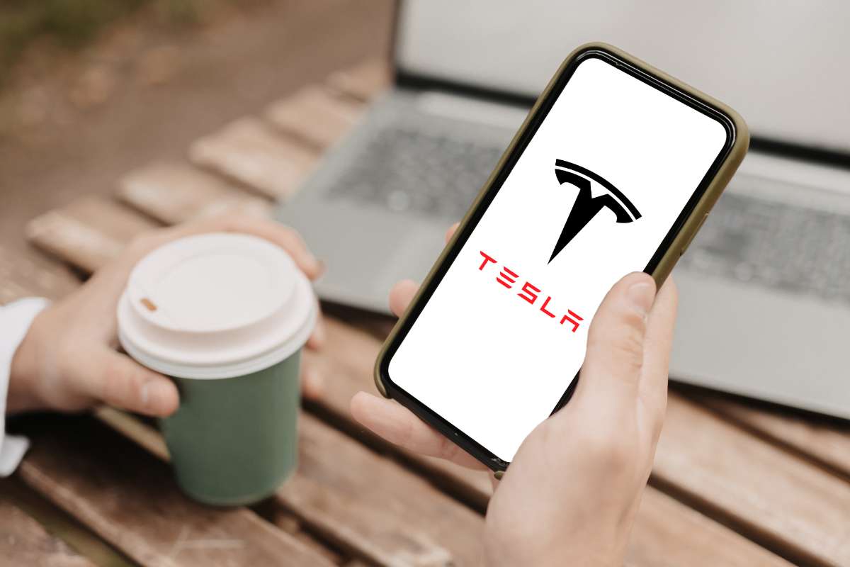 tesla cell phone app showing tesla logo and holding coffee