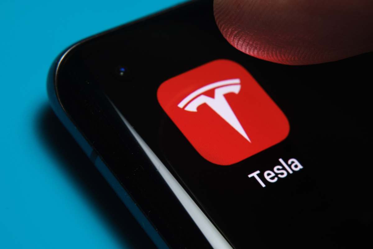 tesla cell phone app installed on cell phone, showing tesla app icon and human thumb