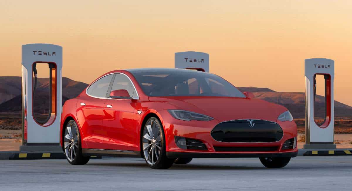red tesla model s in front of tesla superchargers at sunset