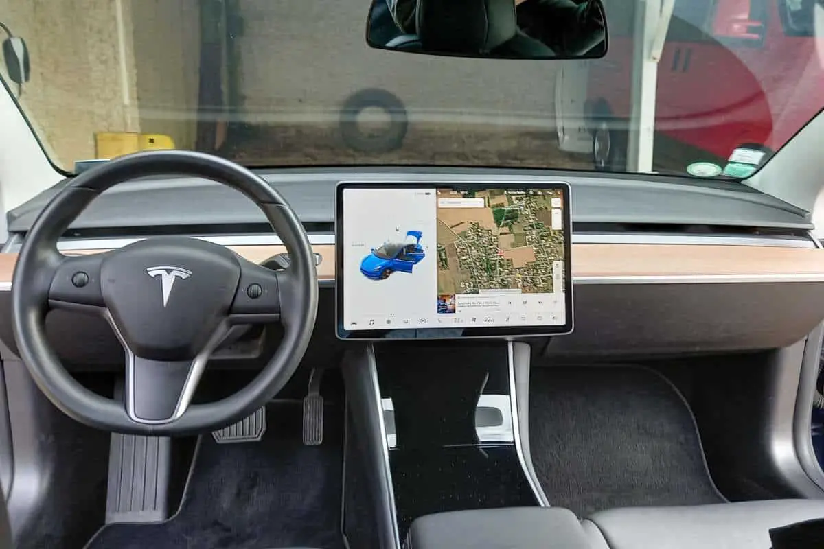 photo of interior of a tesla model 3 showing steering wheel and touchscreen with navigation displayed